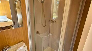 Une cabine de douche fermée par des parois en verre, dotée d’un pommeau de douche à main et d’un robinet fixé au mur.