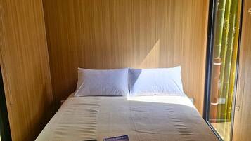 Un lit simple avec un matelas et des oreillers blancs, un livre posé sur le lit et un appareil de climatisation installé au-dessus.