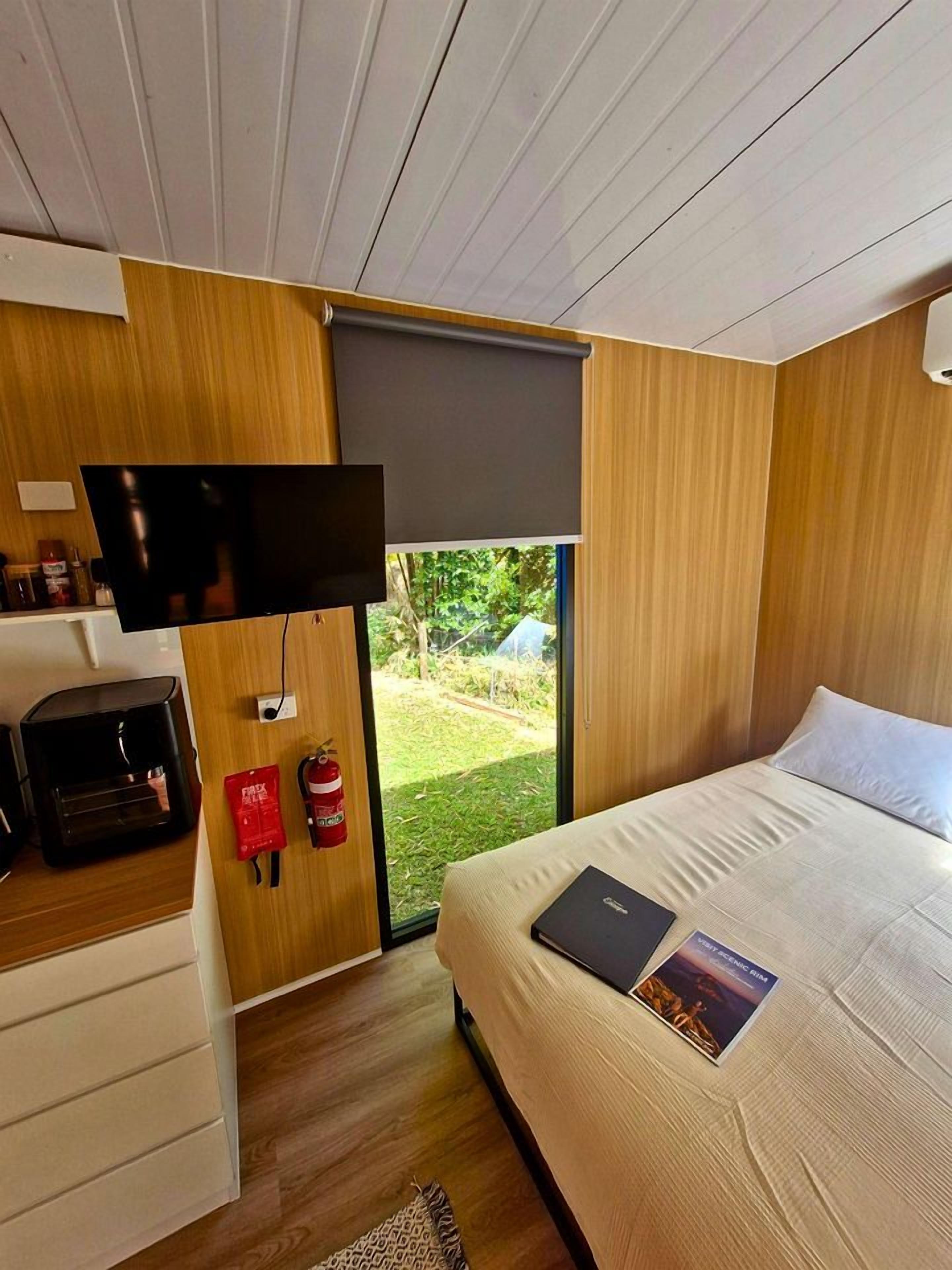 Een moderne slaapkamer met een bed, een aan de muur bevestigde televisie en een klein bureau met een computer.