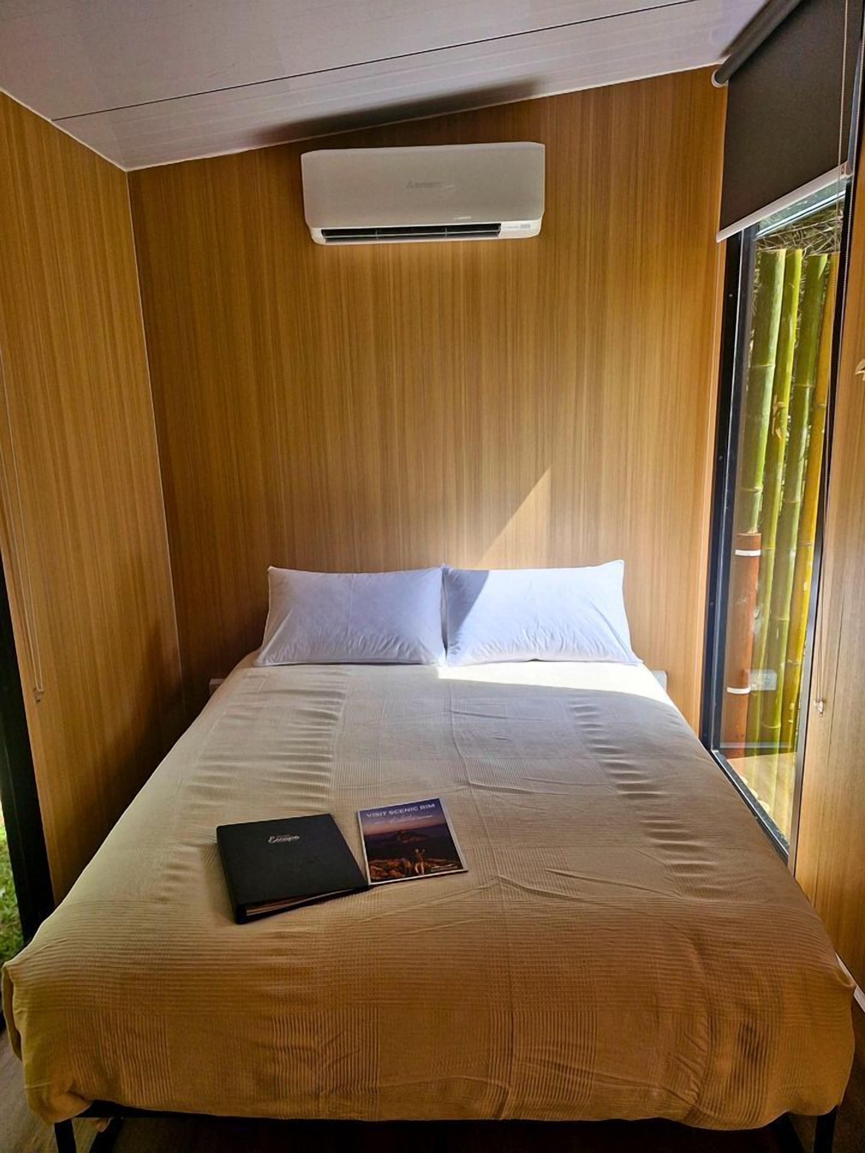 Ein Einzelbett mit weißer Matratze und Kissen, ein Buch auf dem Bett und eine Klimaanlage darüber.