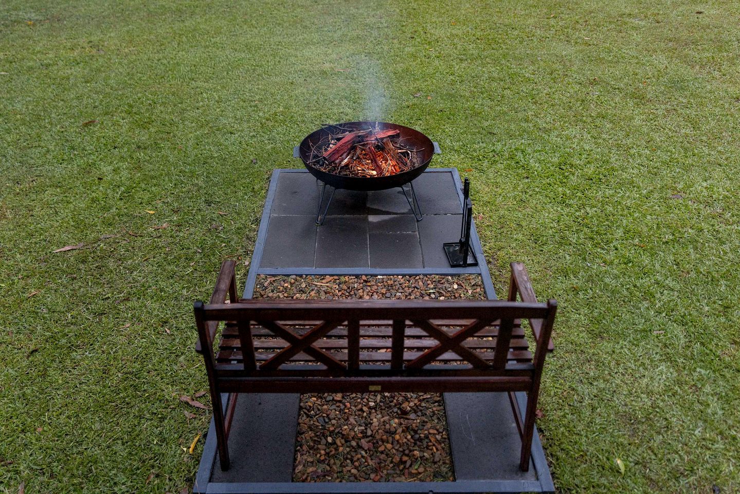 Un barbecue portable, avec un feu allumé sur un support en métal noir, placé sur une pelouse verdoyante.