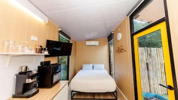Ein kompaktes Zimmer mit Bett, Fernseher, Kaffeemaschine und einer kleinen Küchenzeile.