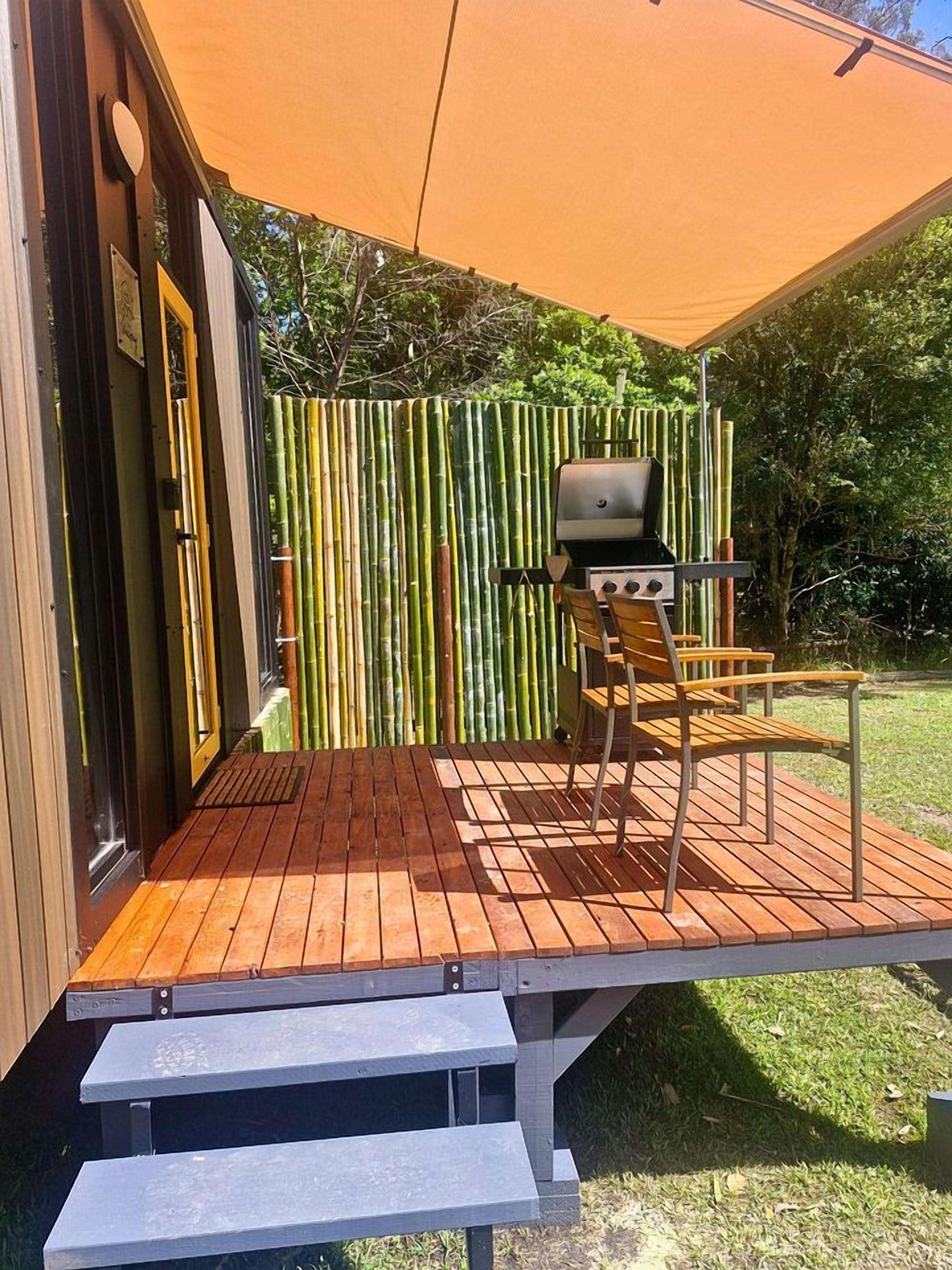 Área externa coberta com churrasqueira, uma cadeira de madeira e um cercado de bambu.