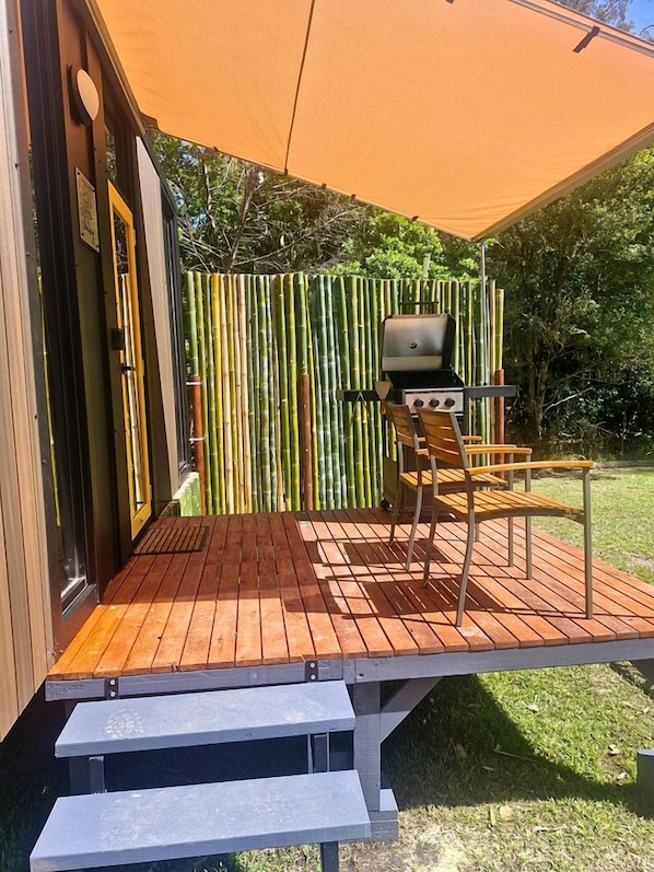 A covered outdoor area with a grill, a wooden chair, and a bamboo fence.