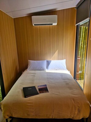 A single bed with a white mattress and pillows, a book on the bed, and an air conditioning unit above it.