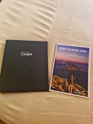 A black folder labeled 'Tiny Away Escape' and a brochure titled 'Visit Scenic Rim' on a textured fabric surface.