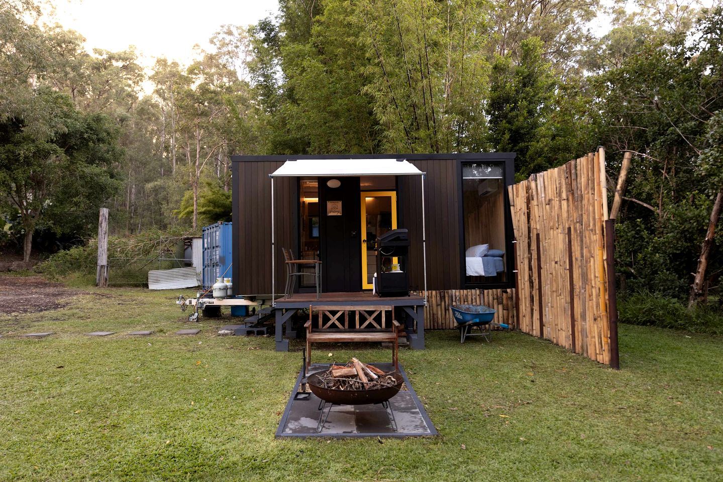 A compact wooden cabin with a deck and a fire pit in the yard.
