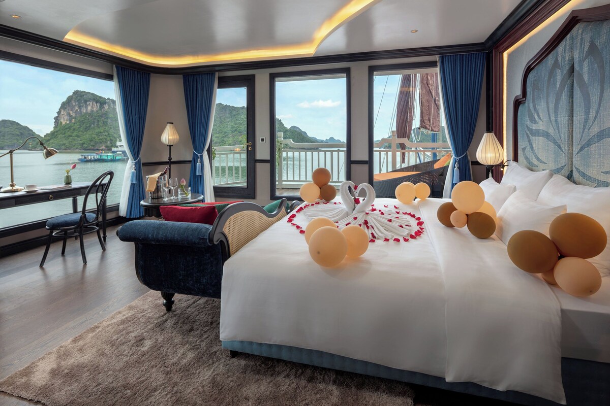 A luxurious bedroom with a large bed, a view of a boat and mountains, and a balcony with curtains.