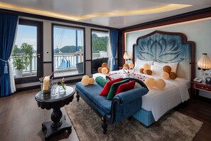 A bedroom with a large bed, a side table, a view of the outdoors, and a balcony.