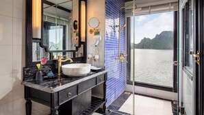 Un baño con lavamanos de mármol, un espejo grande y vista a un lago a través de una puerta de vidrio.
