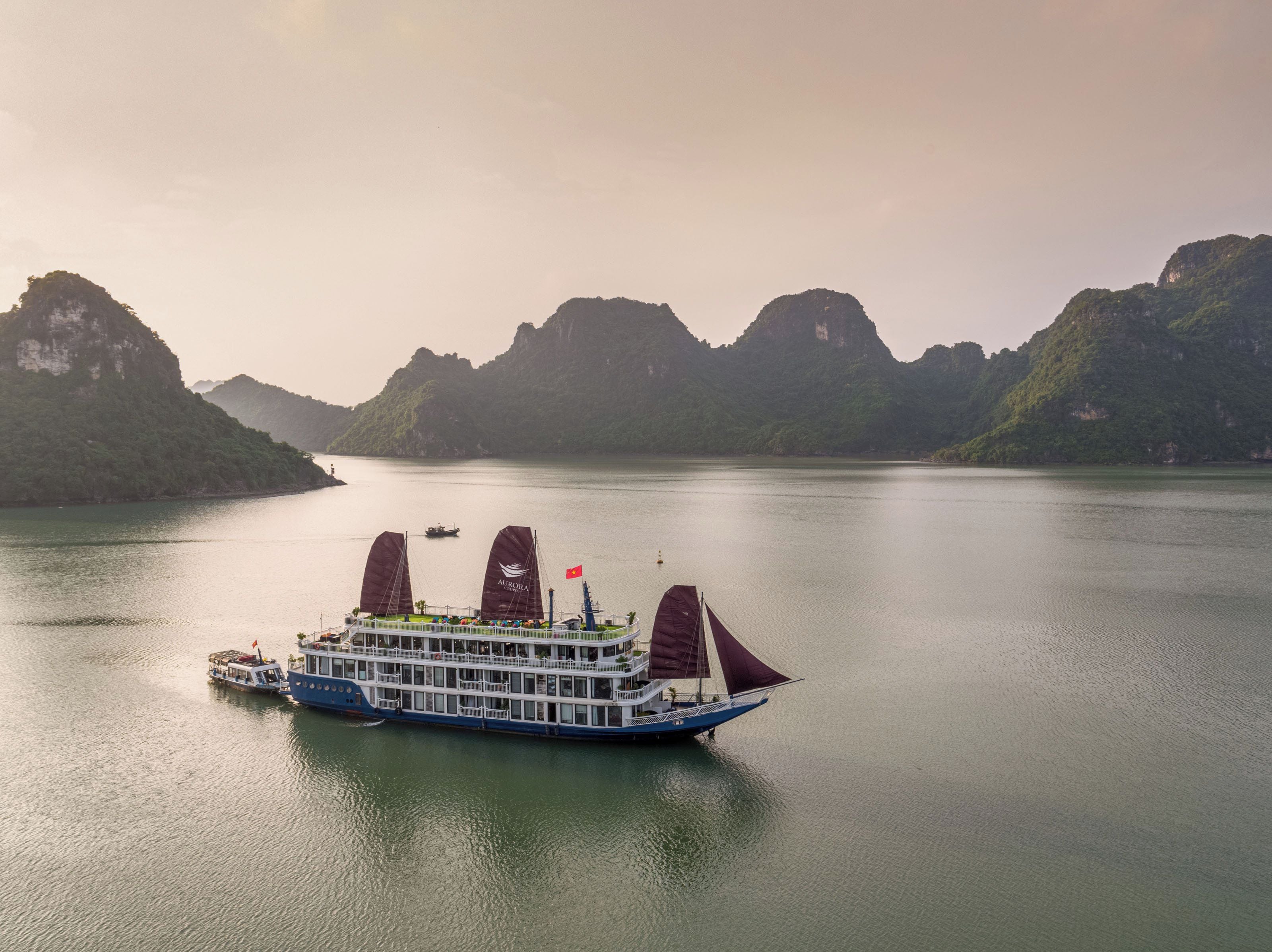 A river cruise ship with multiple decks and a flag, surrounded by lush green hills.