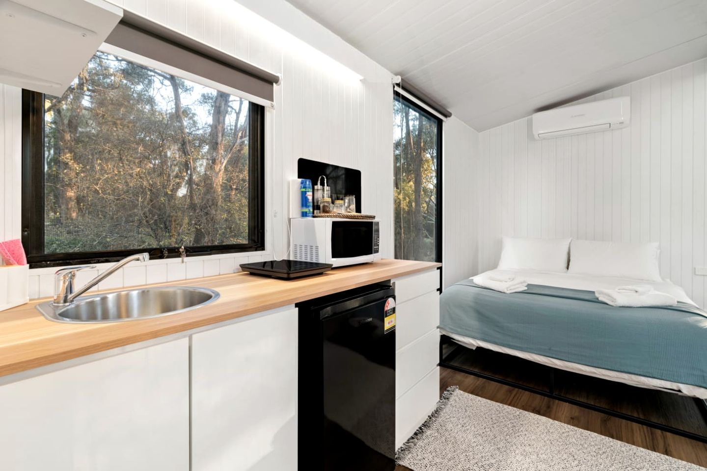 A compact room with a kitchenette, a bed, and a window with a view of trees.
