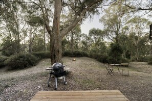 Un área de camping con una parrilla portátil, una terraza de madera y un banco.