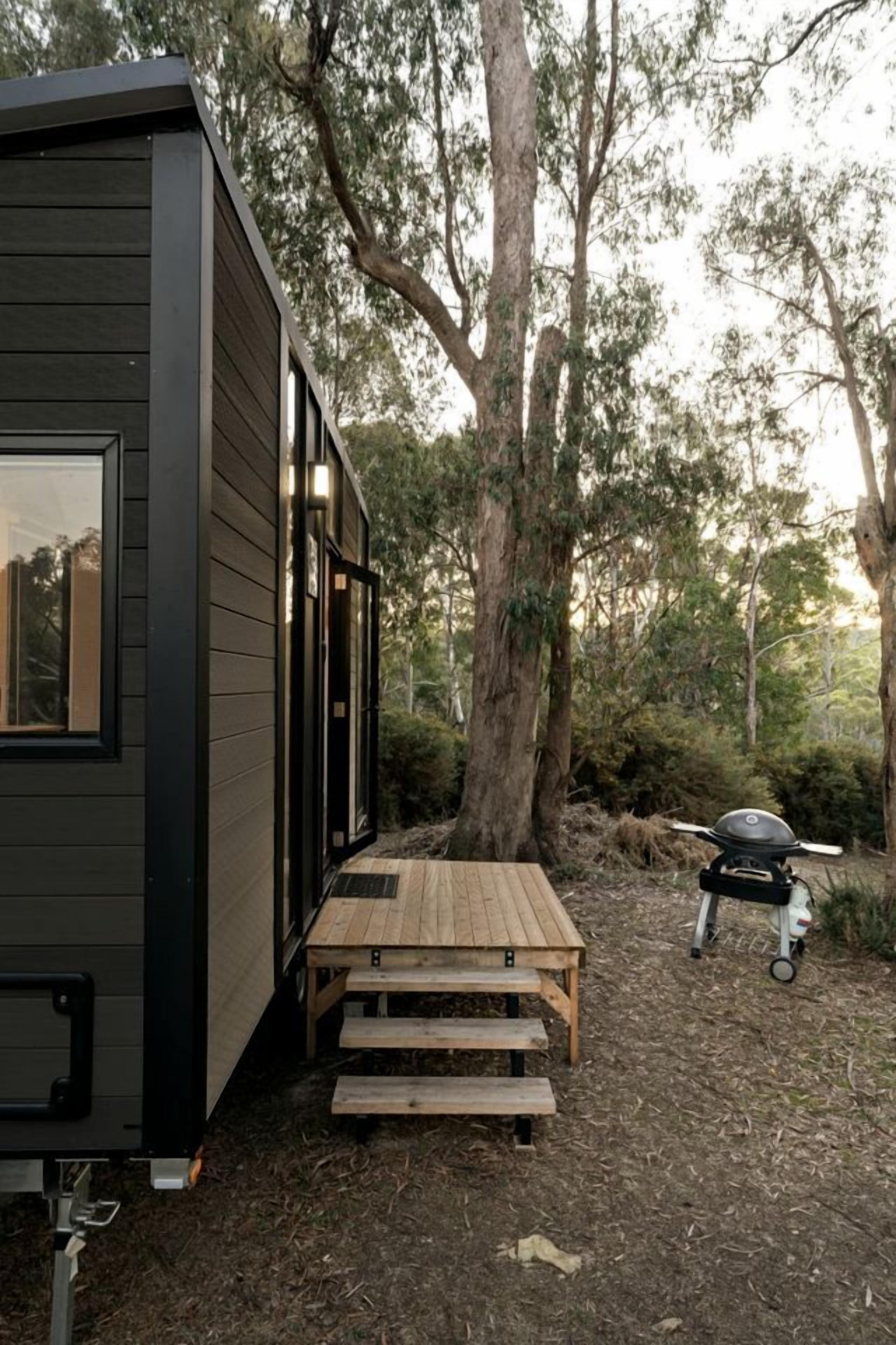 A modern cabin with a wooden deck and a barbecue grill.
