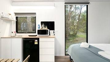 A modern bedroom with a bed, a small kitchenette with a microwave, and a view of the outdoors.