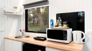 A compact kitchen with a sink, a microwave, a kettle, and a window overlooking a garden.