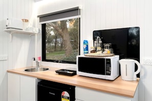 A compact kitchen with a sink, a microwave, a kettle, and a window overlooking a garden.
