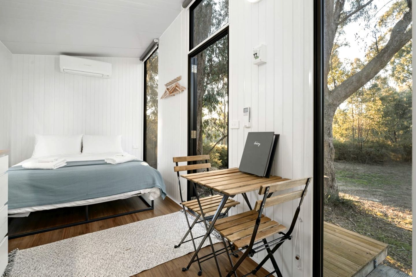 Ein Schlafzimmer mit einem Bett, einem Schreibtisch mit einem Laptop und Blick ins Freie.