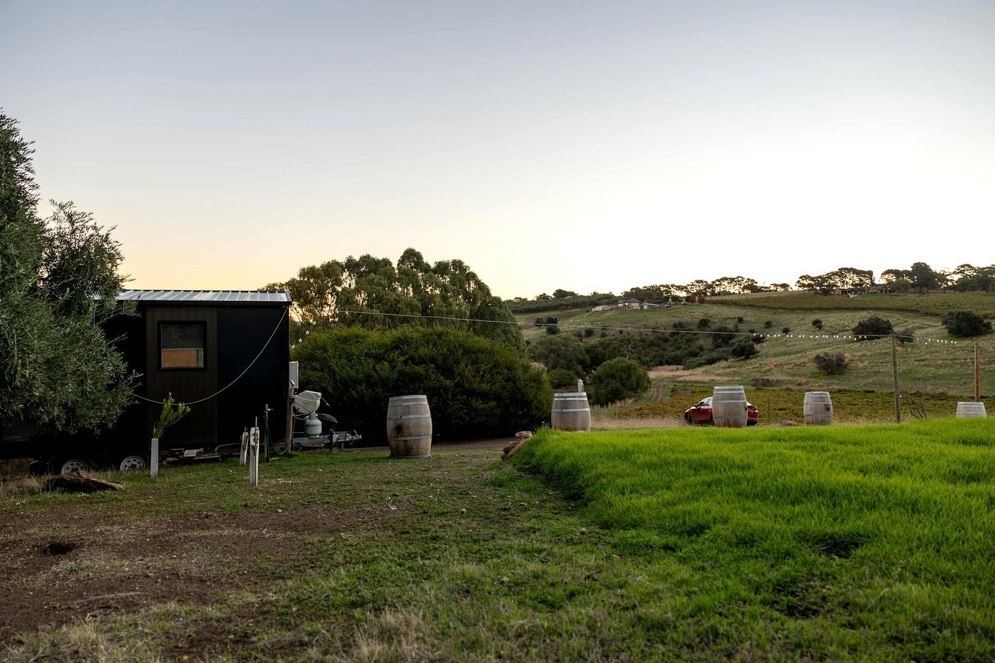 A rural property with a small building, barrels, and a red vehicle.