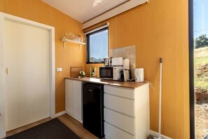 A compact kitchenette with a microwave, coffee maker, and a small shelf with glasses.