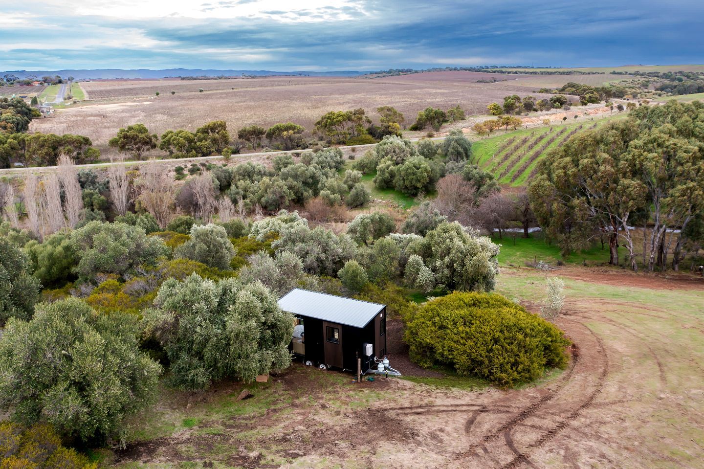 A rural landscape with a small cabin surrounded by dense vegetation and fields.