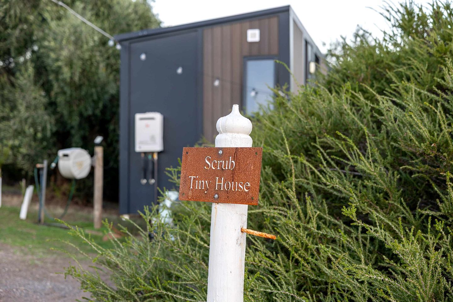 Un cartello con su scritto 'Scrub Tiny House' davanti a un edificio moderno dalla facciata in legno.