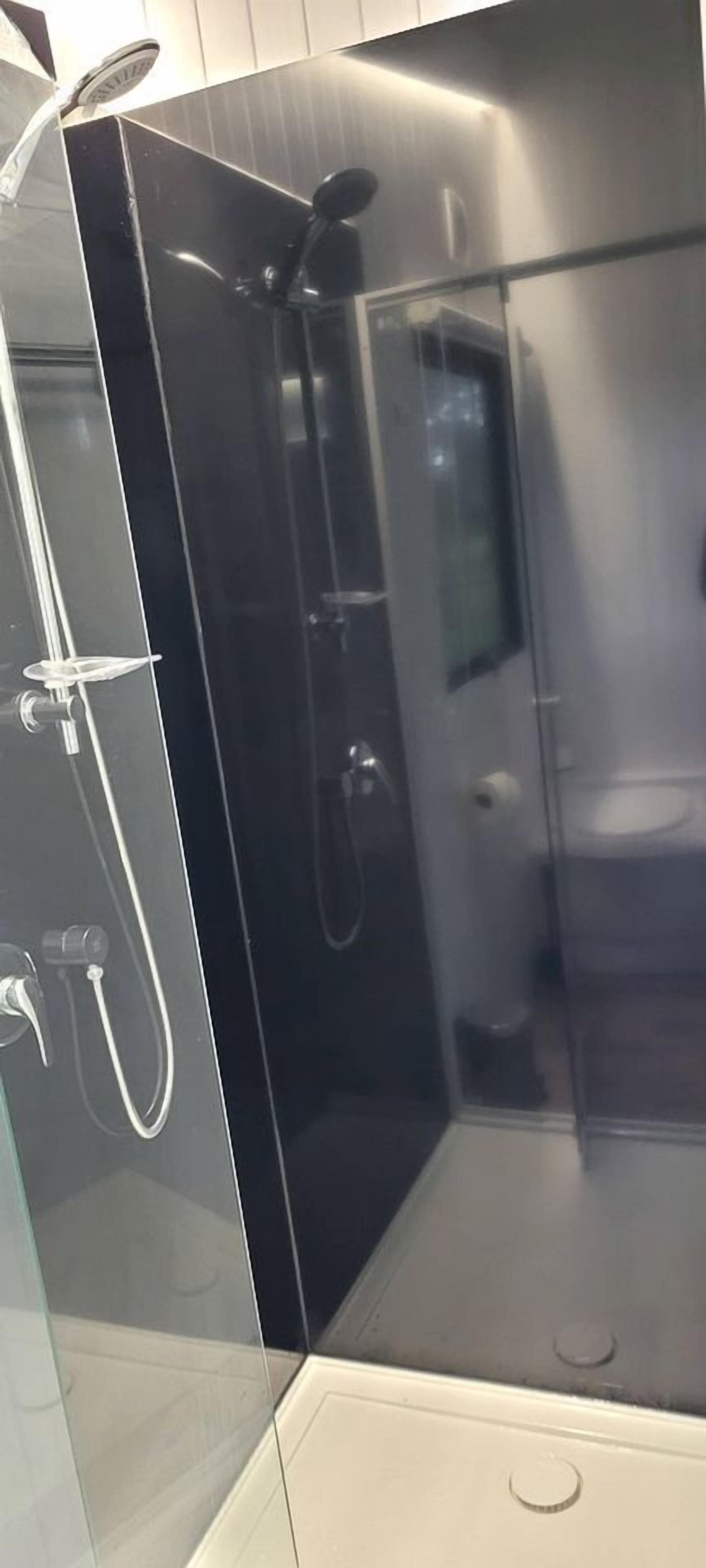 A modern bathroom with a glass shower enclosure, a visible showerhead, and a toilet.