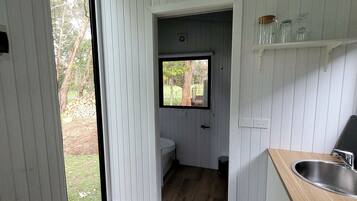 A compact bathroom with a window, a sink, and a small storage shelf.