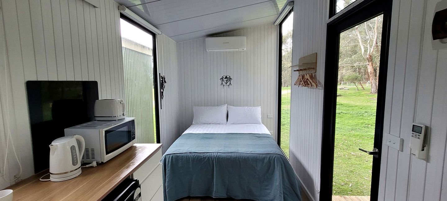 Een kleine kamer met een bed, een televisie, een waterkoker en een magnetron.