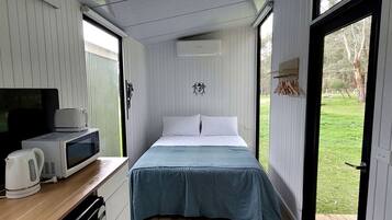 Een kleine kamer met een bed, een televisie, een waterkoker en een magnetron.