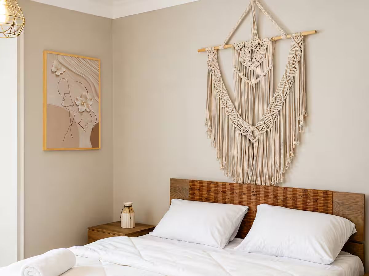 Un lit bien fait, avec du linge de lit blanc, une tête de lit en bois et une décoration murale en macramé.