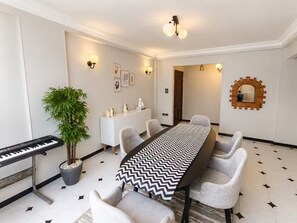 Un espace repas comprenant une longue table, des chaises, un clavier, une plante en pot, des appliques murales et un miroir décoratif.