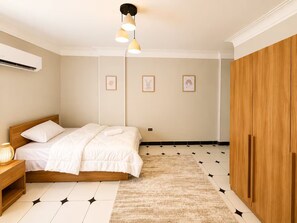 Ein Schlafzimmer mit einem Bett, einer Nachttischlampe, einer Wandklimaanlage, gerahmten Bildern und einem Kleiderschrank.