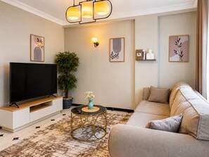Ein modernes Wohnzimmer mit Flachbildfernseher, einer Couch, einem Couchtisch und dekorativen Wandbildern.