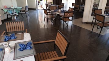 Une salle à manger avec des tables dressées pour le service, des chaises disposées autour, et une personne se tenant près de l’entrée.