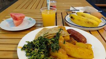 Una mesa de madera con un plato de comida, un vaso de jugo de naranja y un plátano sobre un mantel.