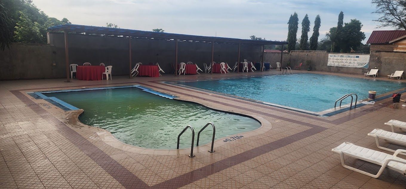 A swimming pool with two separate sections, a covered seating area with tables and chairs, and a tiled walkway.