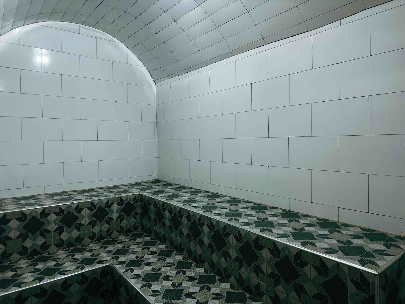 A bathroom with white tiled walls, a green and white patterned floor, and a curved ceiling.