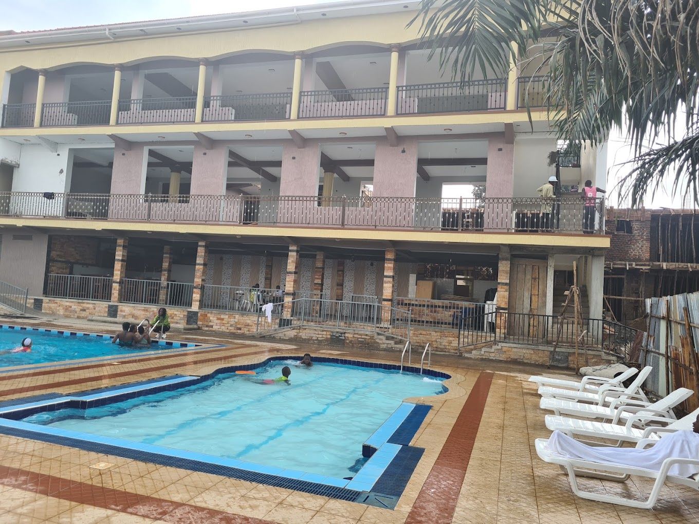 A pool area with multiple swimming pools and lounge chairs, surrounded by a building with balconies.