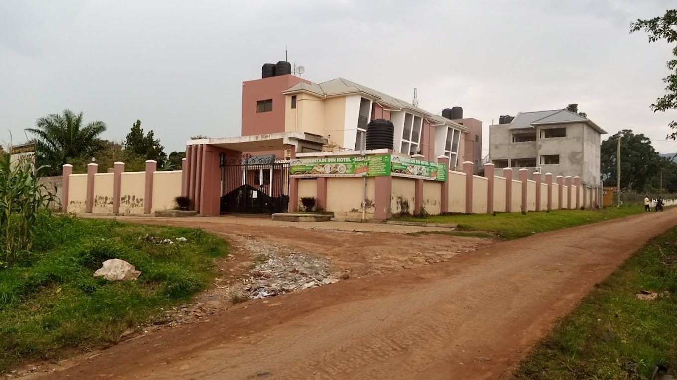 A hotel with a gated entrance, a dirt road leading to it, and a signboard advertising the hotel.
