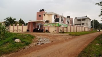 A hotel with a gated entrance, a dirt road leading to it, and a signboard advertising the hotel.