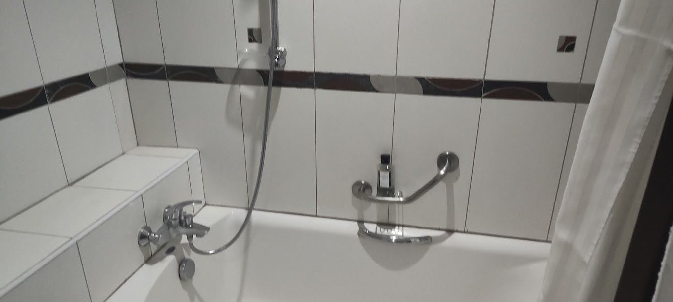 A bathroom with white tiled walls, a shower with a handheld showerhead, and a bathtub with a handheld showerhead.
