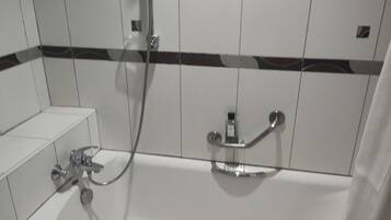 A bathroom with white tiled walls, a shower with a handheld showerhead, and a bathtub with a handheld showerhead.