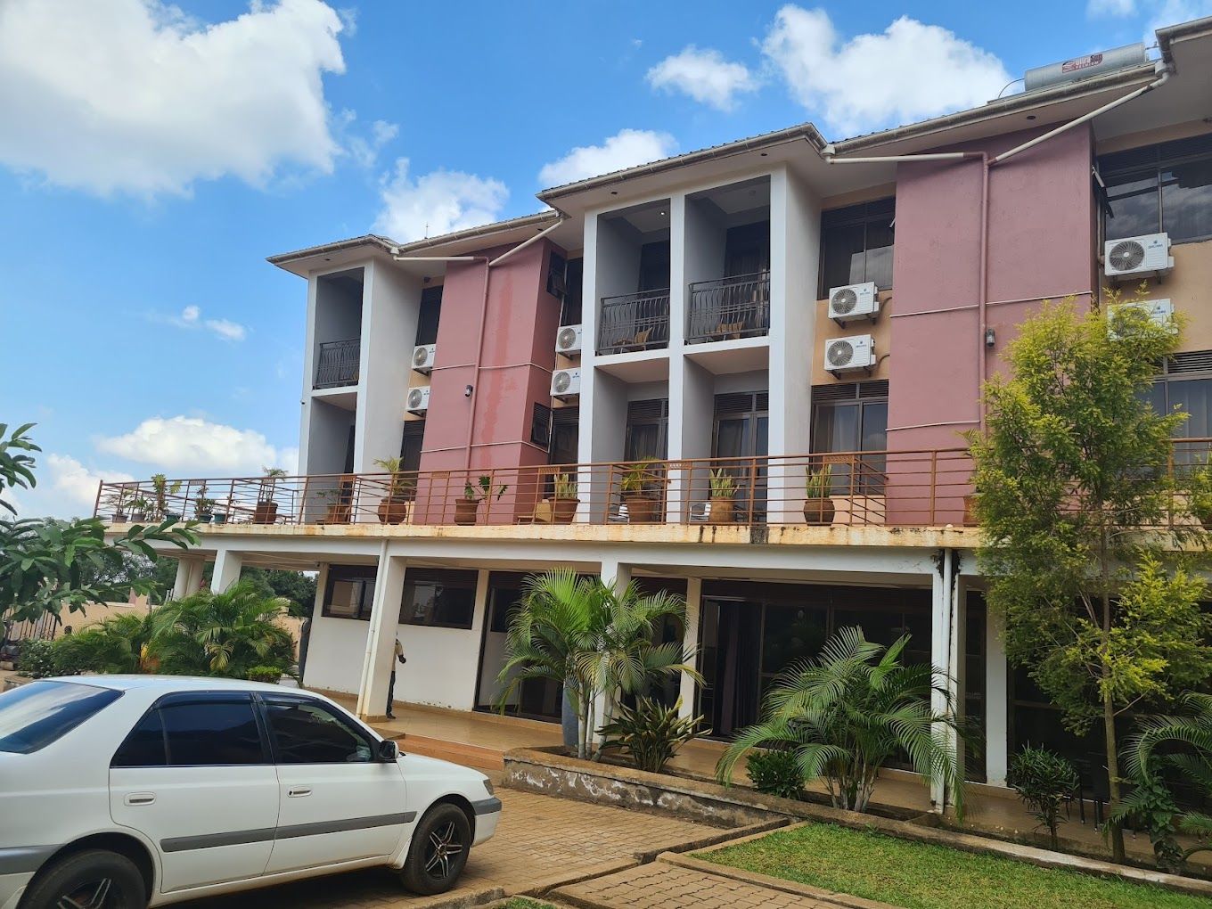 A multi-story building with balconies, air conditioning units, and a car parked in front.