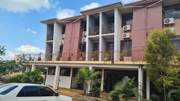 Un immeuble à plusieurs étages doté de balcons, de climatiseurs et d’une voiture garée devant.