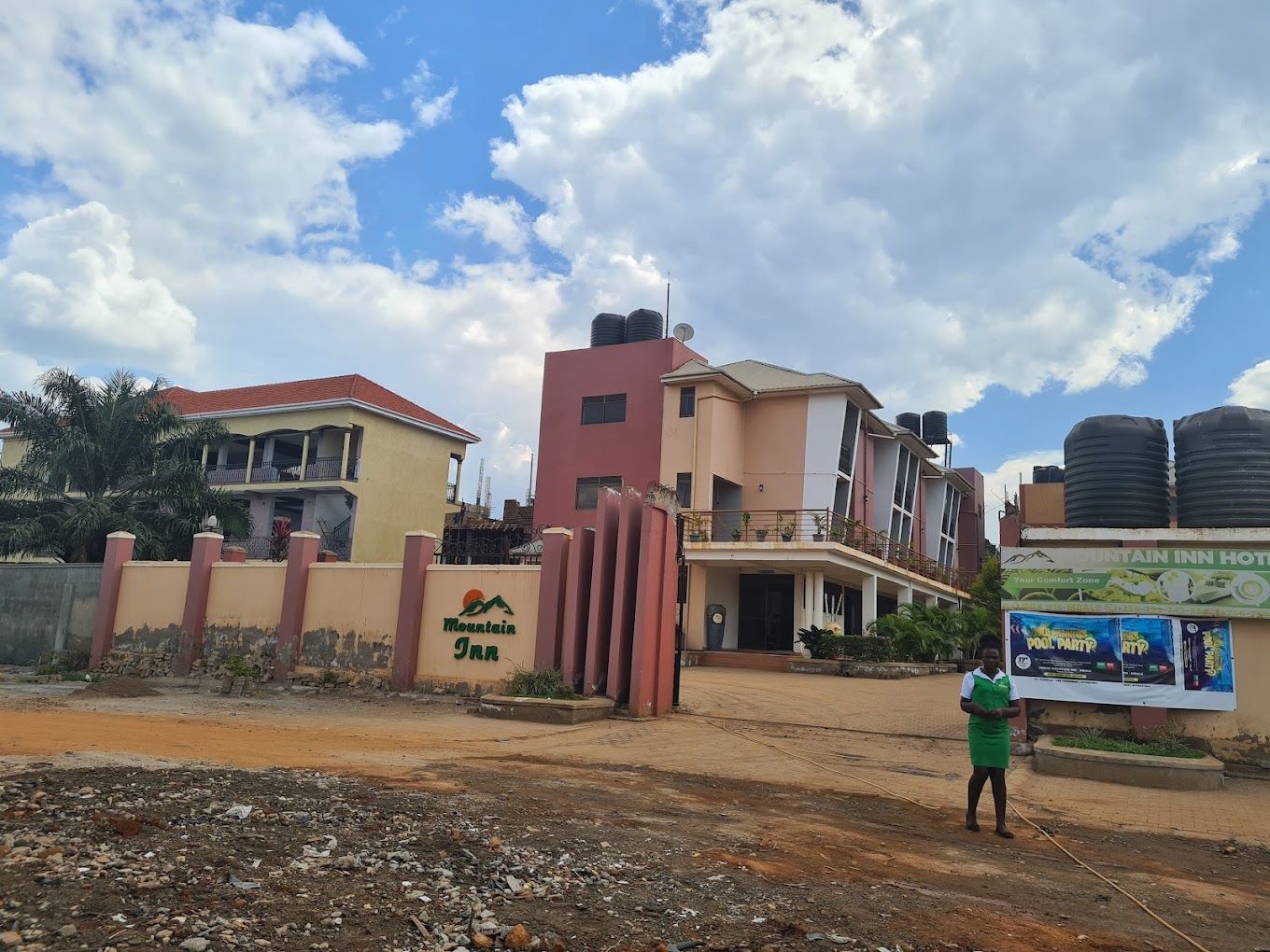A hotel with a gated entrance, a signboard, and a person standing in front.