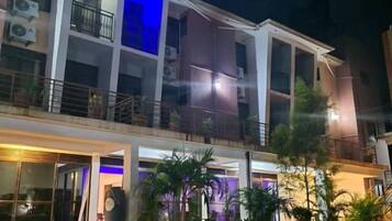 Un edificio de varios pisos con balcones, un área de entrada empaveda e iluminación exterior.