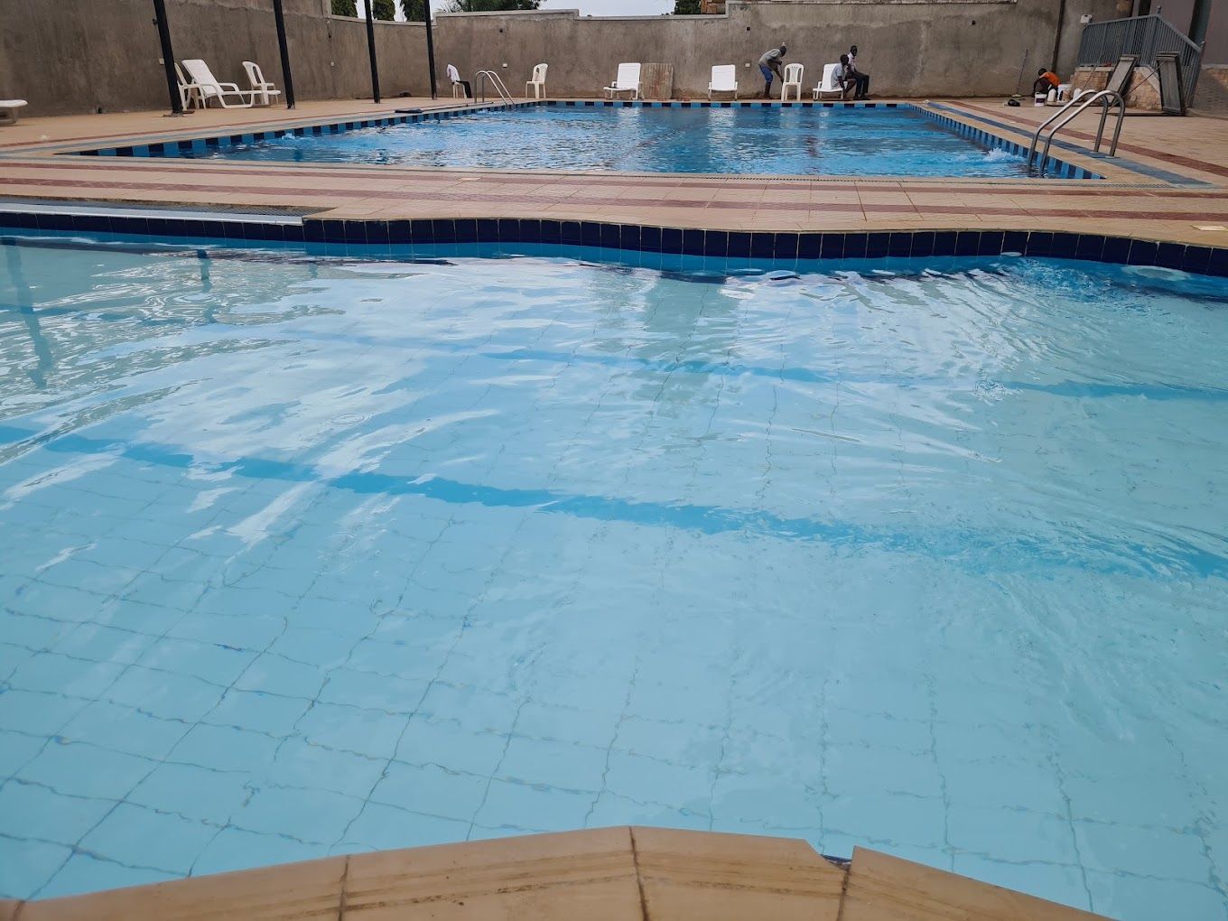 Une piscine à l’eau d’un bleu cristallin, entourée de chaises longues blanches et bordée d’une terrasse carrelée.