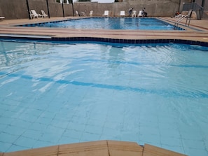 Una piscina con agua azul cristalina, rodeada de sillones blancos y un suelo de baldosas.