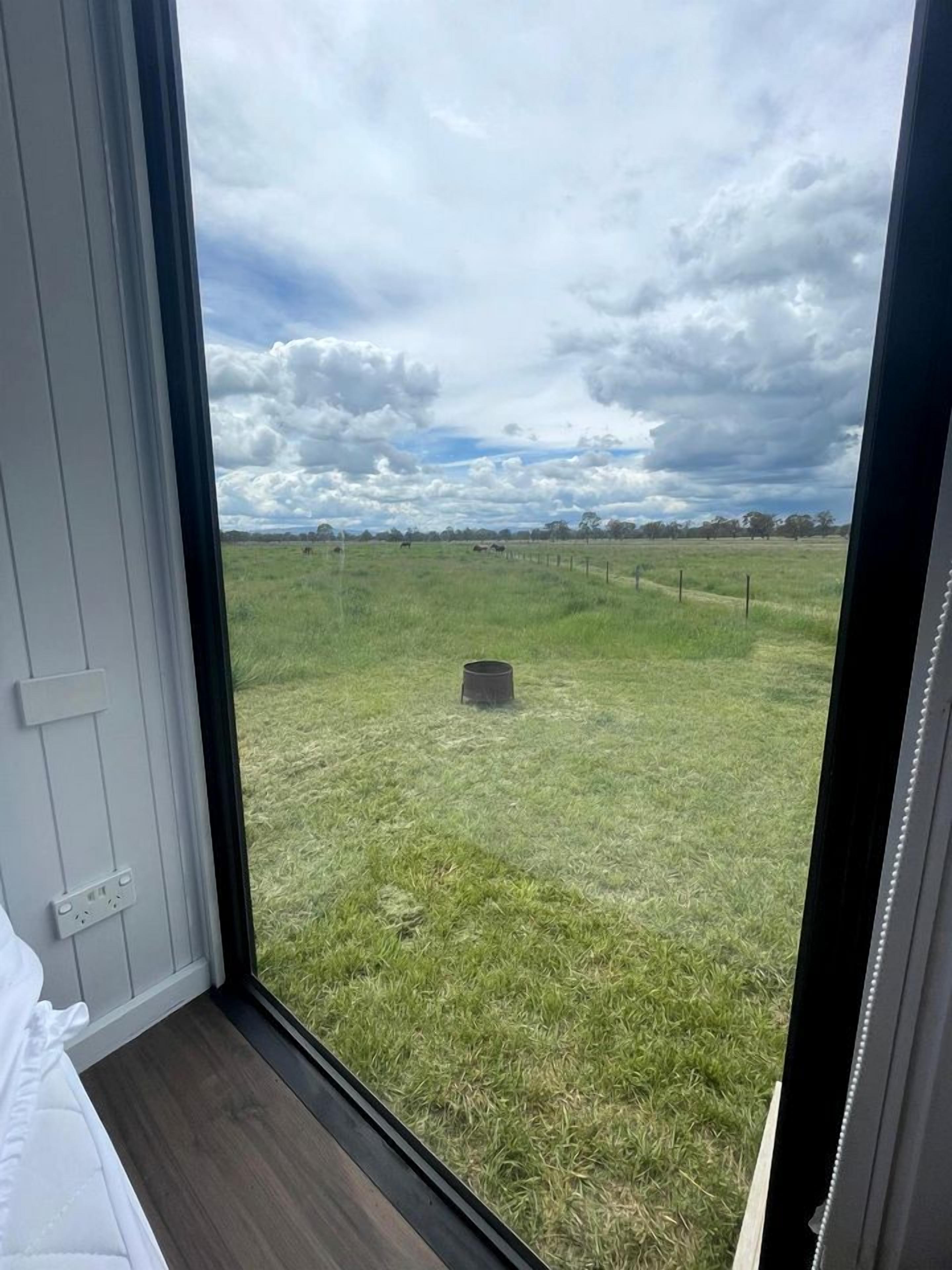 A room with a large window overlooking a grassy field and a cloudy sky.
